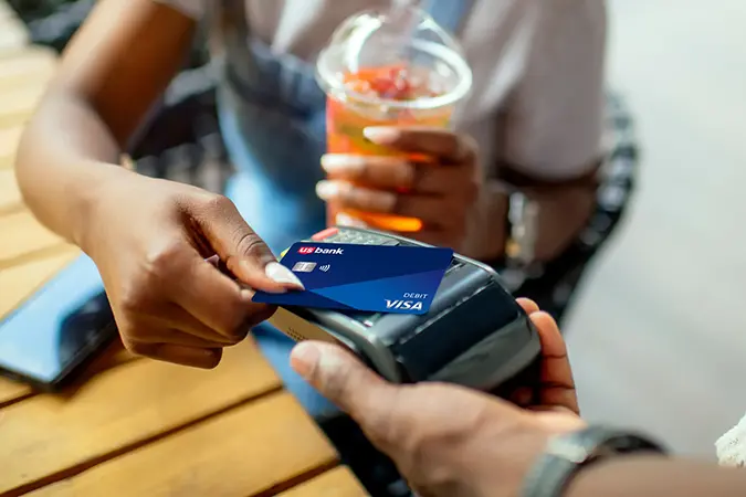 Person making a payment by tapping a debit card on a payment terminal at a counter.